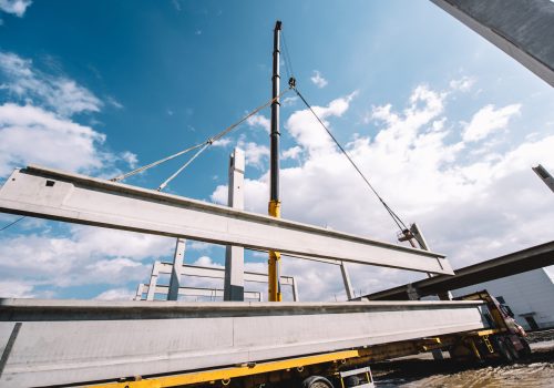 Guindaste industrial pesado levantando vigas e pilares de cimento pré-moldado no canteiro de obras