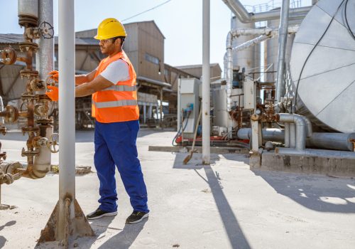 Trabalhador da construção civil concentrado usando colete de construção e capacete, mantendo o equipamento de distribuição na fábrica da indústria pesada